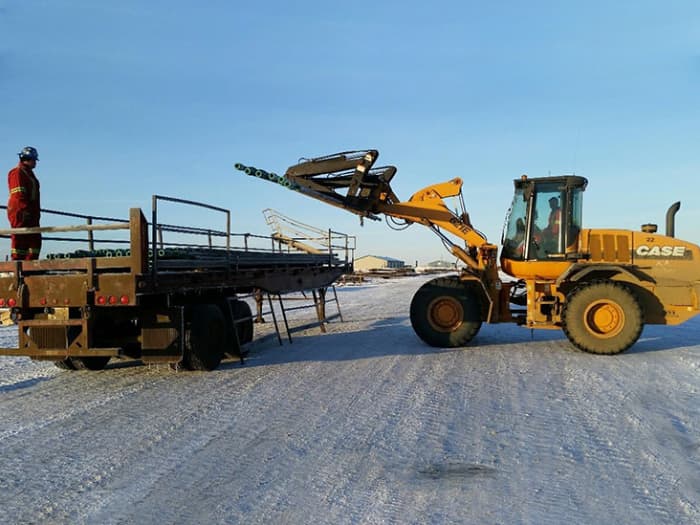 Case front-loader loading pipe onto back of trailer for delivery