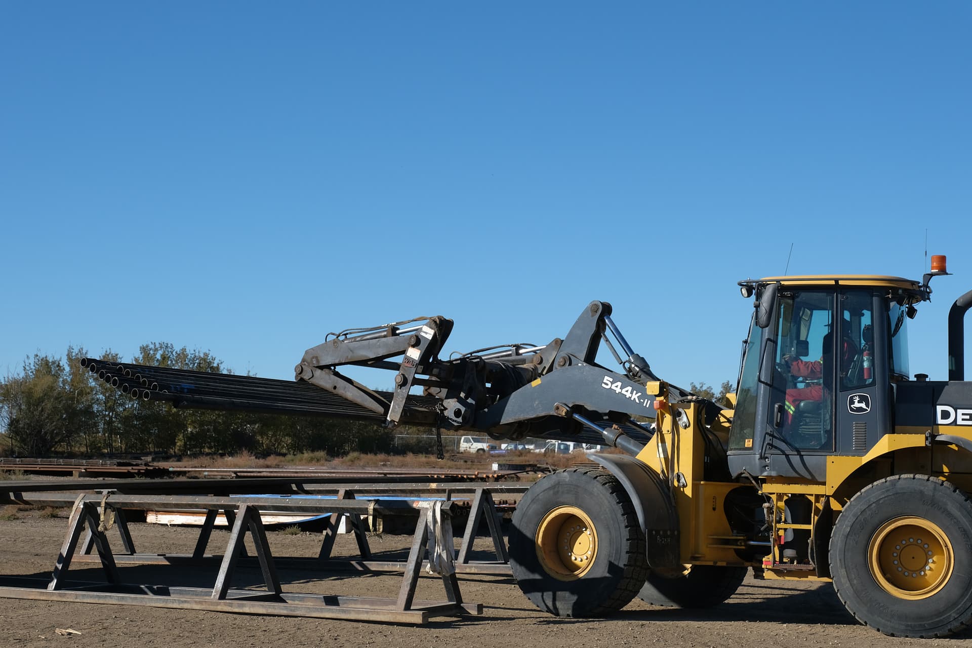 Case front-loader loading pipe onto back of trailer for delivery